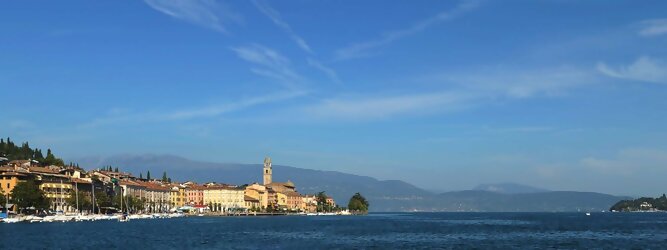 Trip Großbritannien beliebte Urlaubsziele am Gardasee -  Mit einer Fläche von 370 km² ist der Gardasee der größte See Italiens. Es liegt am Fuße der Alpen und erstreckt sich über drei Staaten: Lombardei, Venetien und Trentino. Die maximale Tiefe des Sees beträgt 346 m, er hat eine längliche Form und sein nördliches Ende ist sehr schmal. Dort ist der See von den Bergen der Gruppo di Baldo umgeben. Du trittst aus deinem gemütlichen Hotelzimmer und es begrüßt dich die warme italienische Sonne. Du blickst auf den atemberaubenden Gardasee, der in zahlreichen Blautönen schimmert - von tiefem Dunkelblau bis zu funkelndem Türkis. Majestätische Berge umgeben dich, während die Brise sanft deine Haut streichelt und der Duft von blühenden Zitronenbäumen deine Nase kitzelt. Du schlenderst die malerischen, engen Gassen entlang, vorbei an farbenfrohen, blumengeschmückten Häusern. Vereinzelt unterbricht das fröhliche Lachen der Einheimischen die friedvolle Stille. Du fühlst dich wie in einem Traum, der nicht enden will. Jeder Schritt führt dich zu neuen Entdeckungen und Abenteuern. Du probierst die köstliche italienische Küche mit ihren frischen Zutaten und verführerischen Aromen. Die Sonne geht langsam unter und taucht den Himmel in ein leuchtendes Orange-rot - ein spektakulärer Anblick.